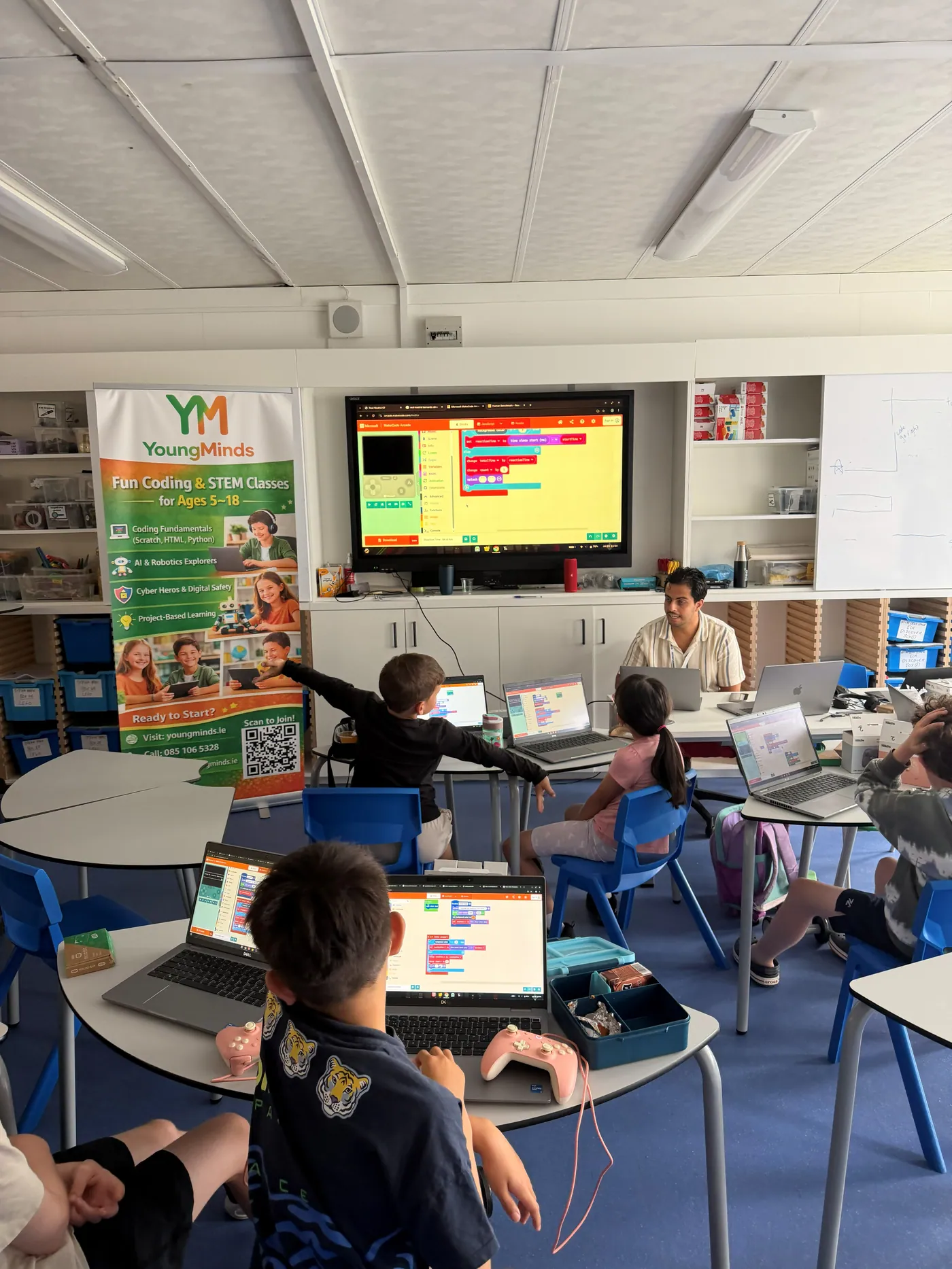 Campers coding a MakeCode Arcade game on laptops while a mentor looks on