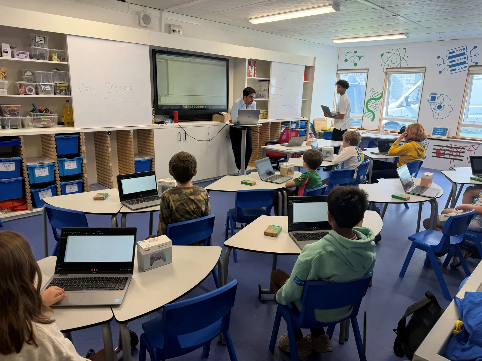 A mentor leading a build block from the front of the room while campers work at their laptops