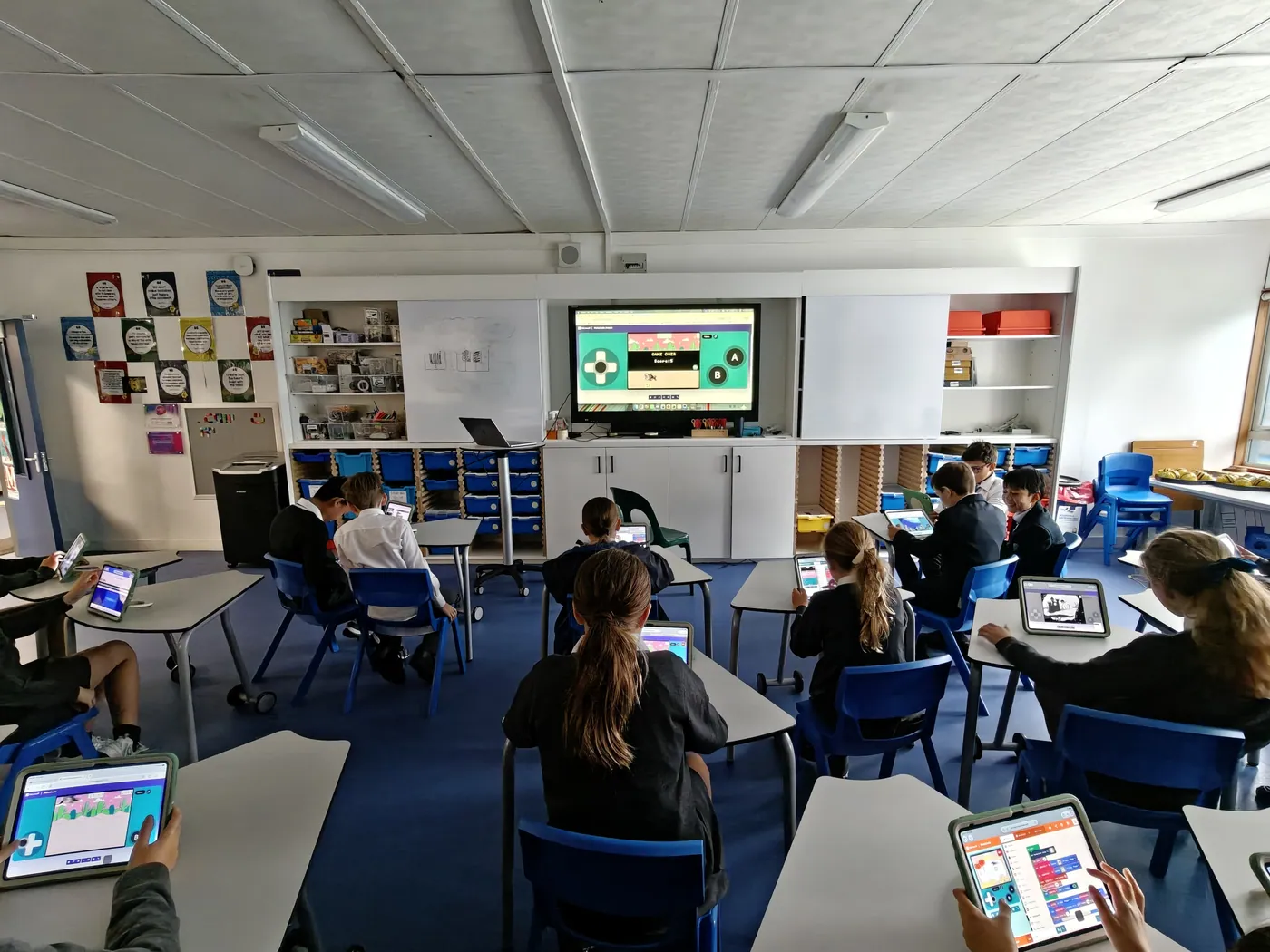Students building a MakeCode Arcade game on tablets with the game on the big screen