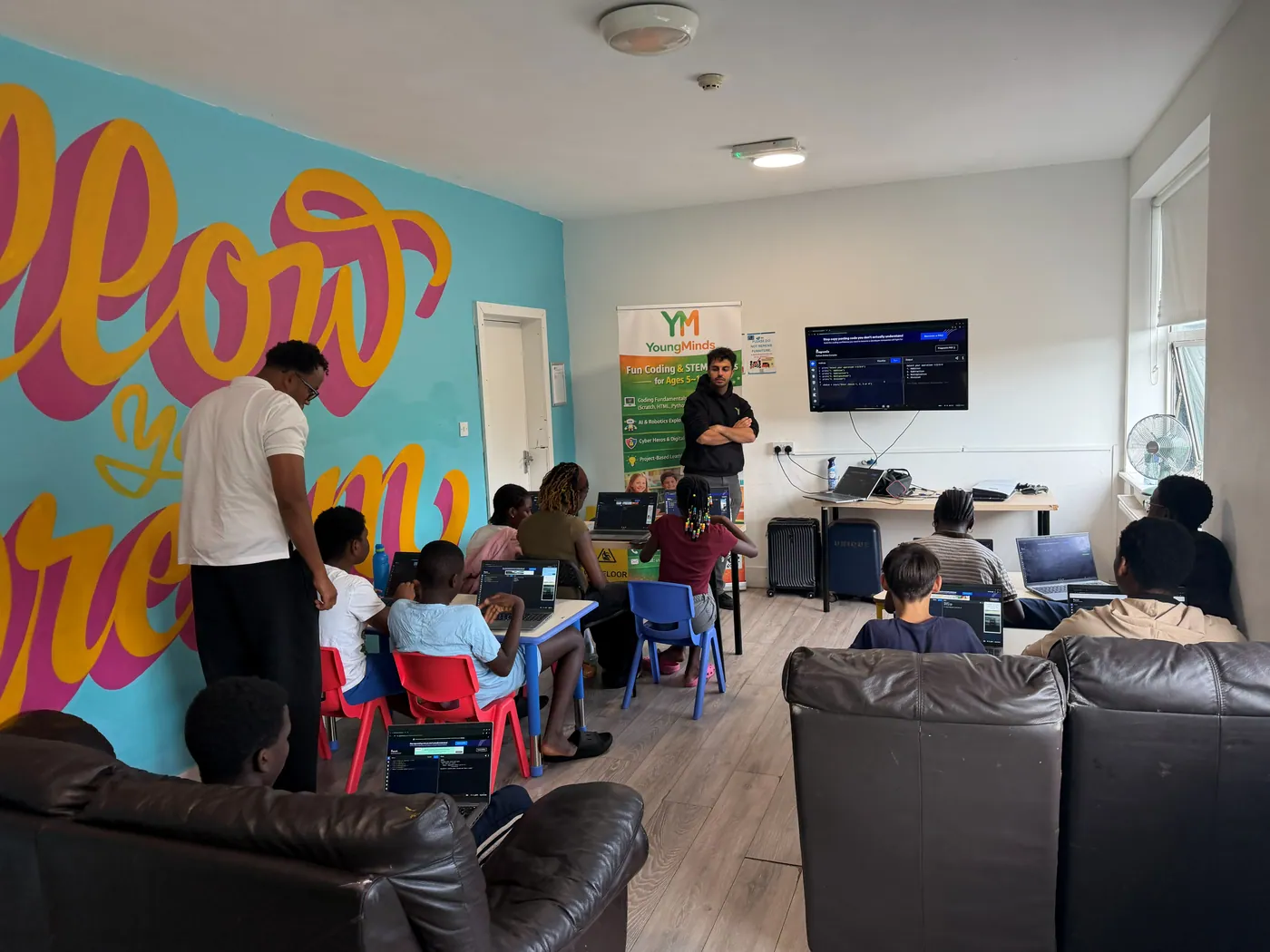 A mentor leading a Python lesson at a community partnership session, with students at laptops