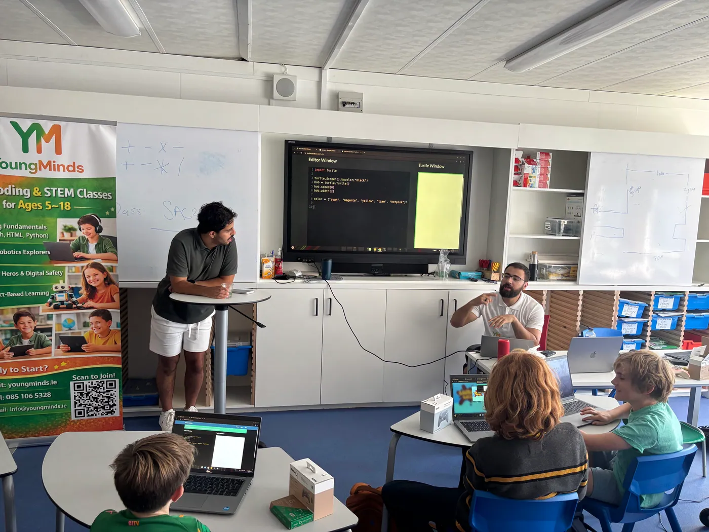 Two mentors teaching Python Turtle graphics to students at laptops