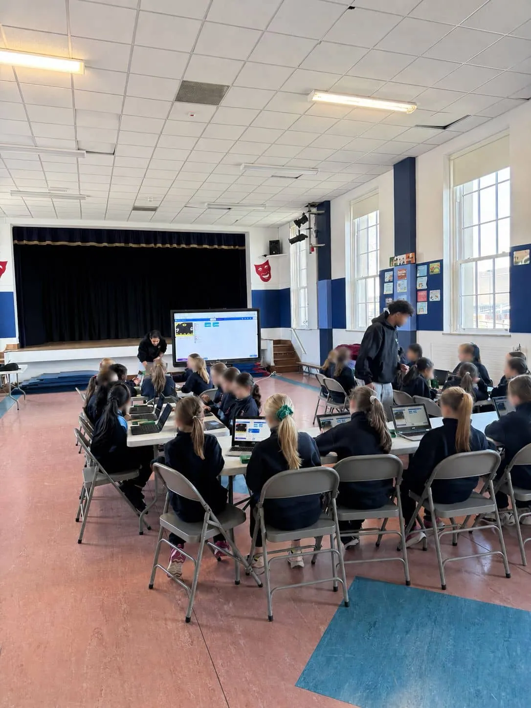 Primary school students coding on laptops with Scratch displayed on the projector